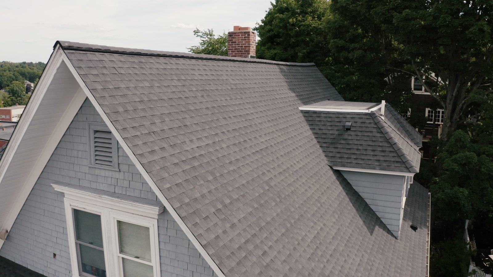 Gray asphalt shingle roof with a dormer window on a sunny day.