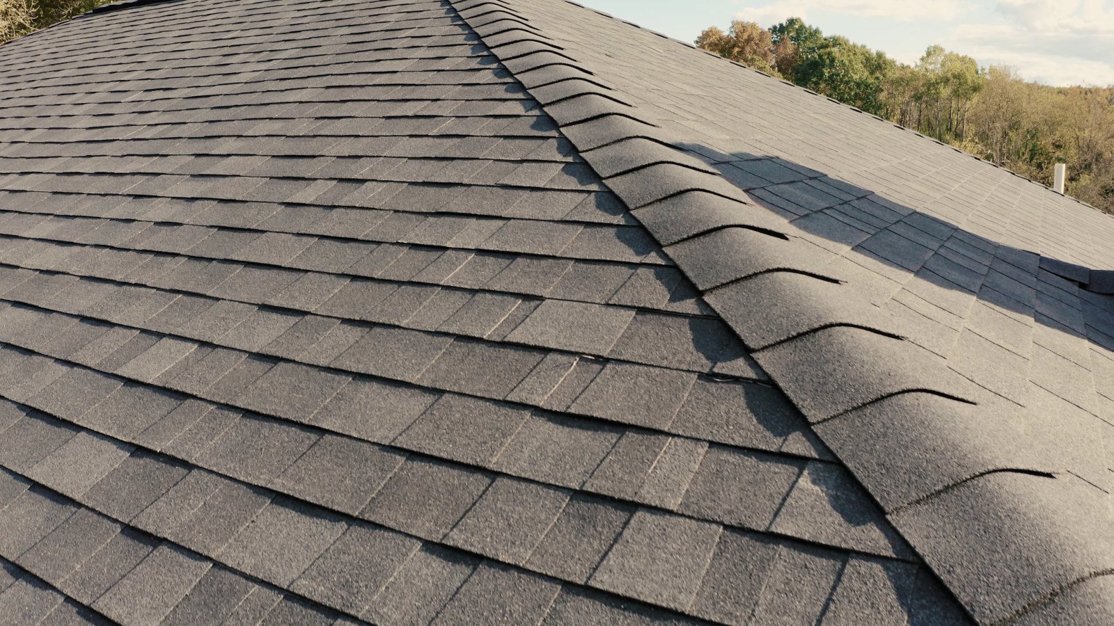 Gray architectural asphalt shingle roof with a dormer window on a sunny day.